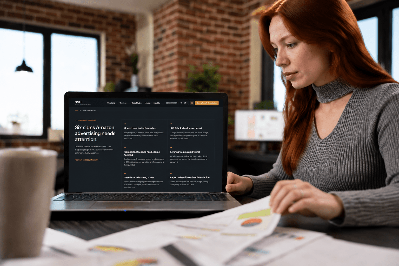 Amazon PPC agency reviewing an account diagnosis on a laptop beside printed performance charts