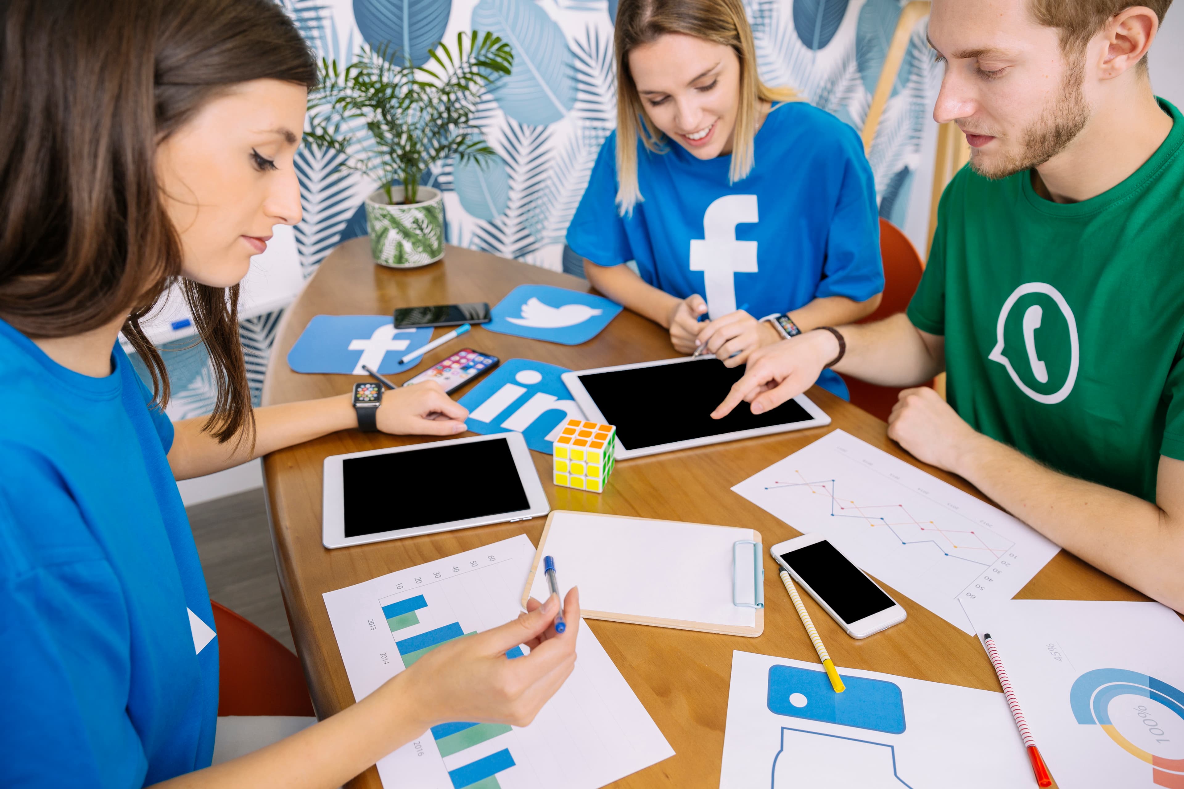 A social media team reviewing campaign charts on tablets, with Facebook, Twitter and LinkedIn icons on the table.