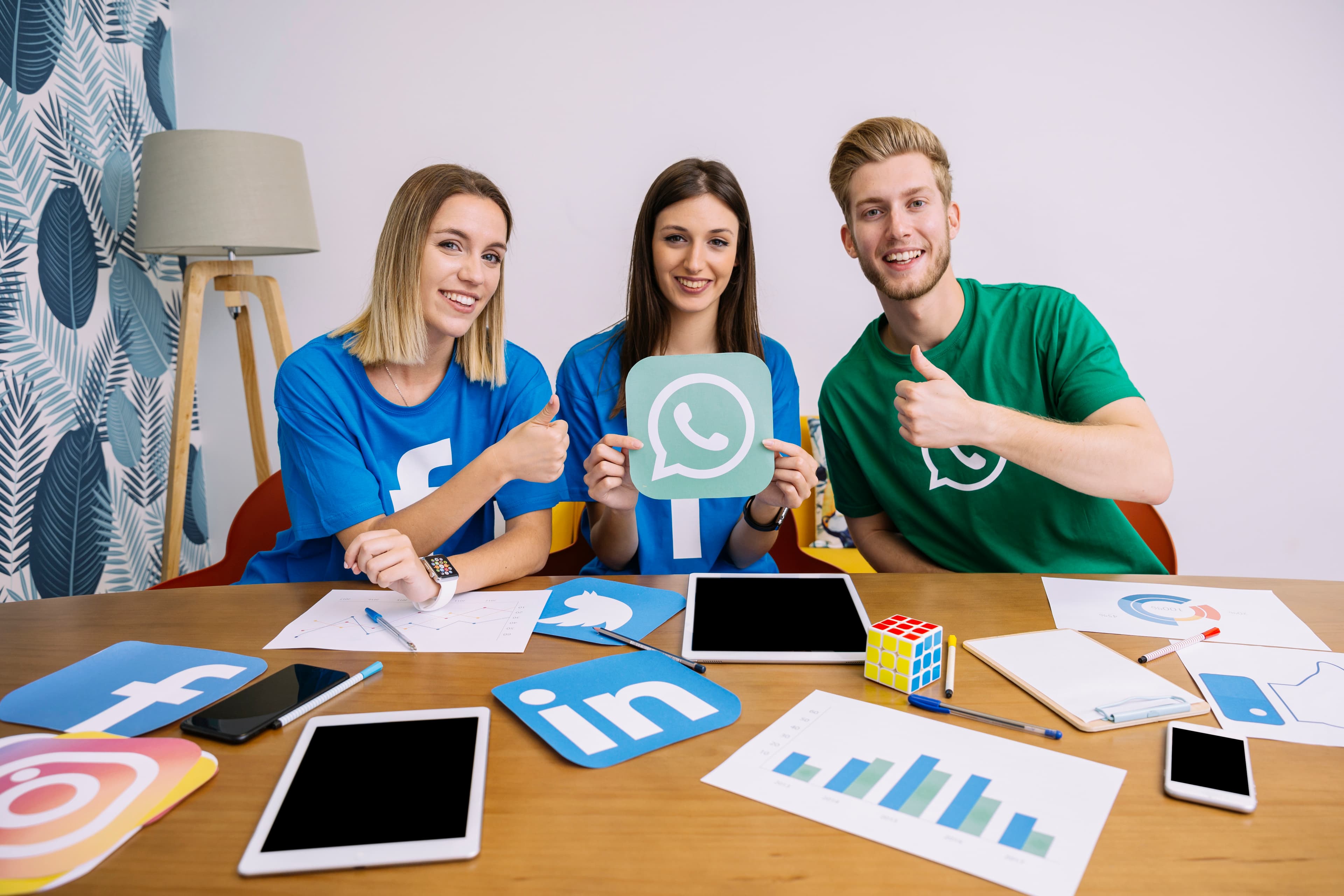 Three social media marketers giving a thumbs up at a planning table covered in Instagram, Facebook and LinkedIn icons.