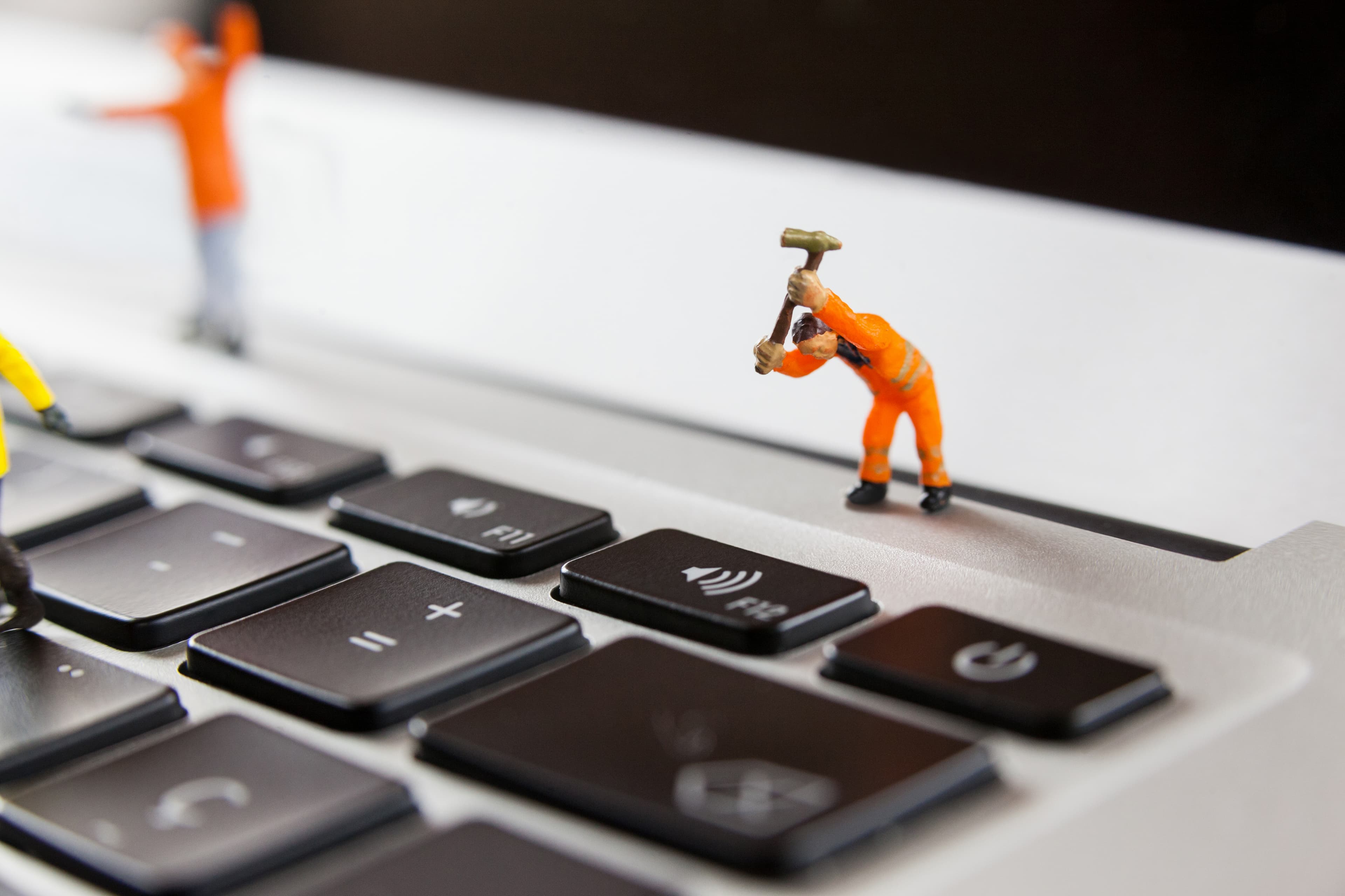 Miniature maintenance figures at work on a laptop keyboard, standing in for the ongoing repair work covered by the warranty.